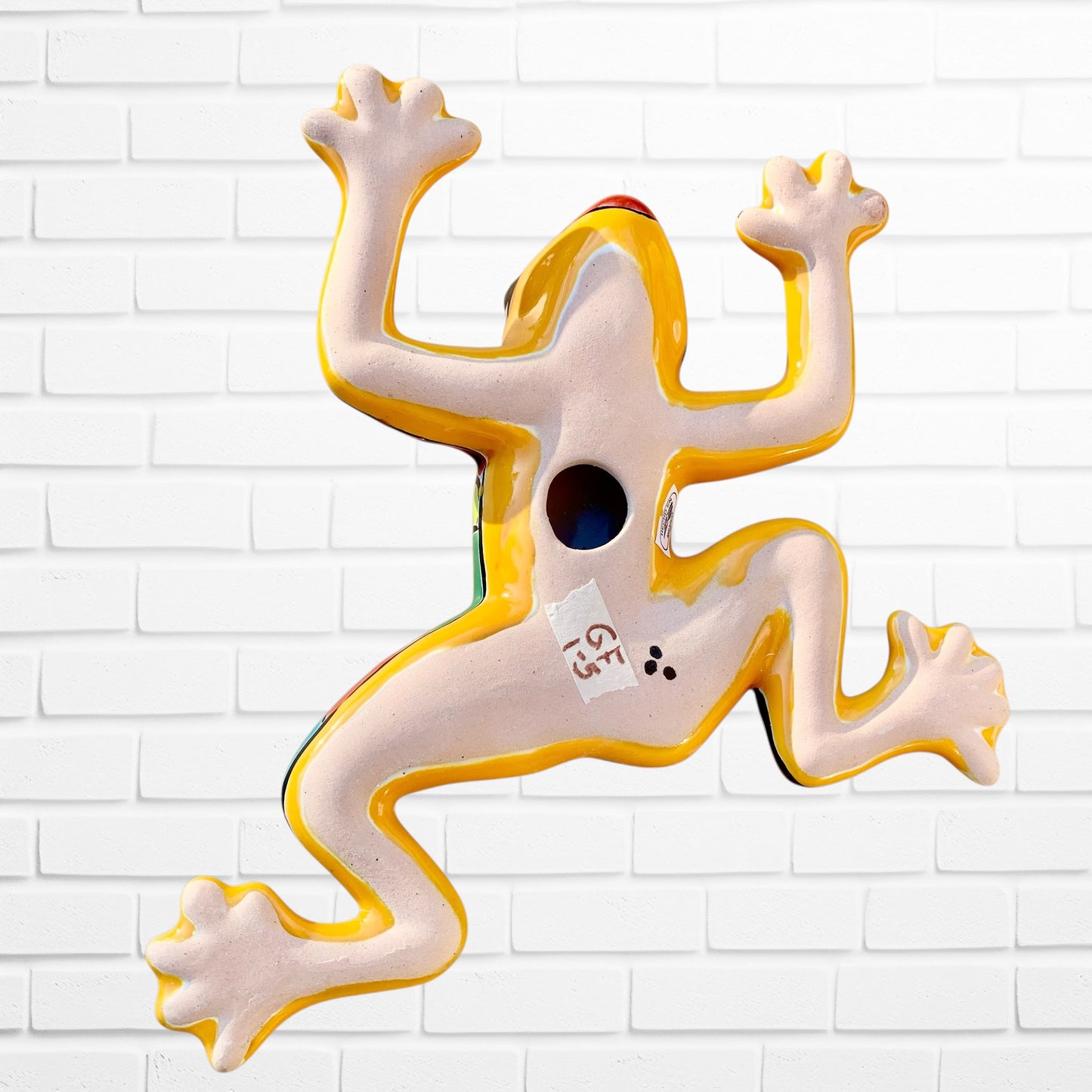 Decorative wall art of a stylized frog on a white brick wall background back