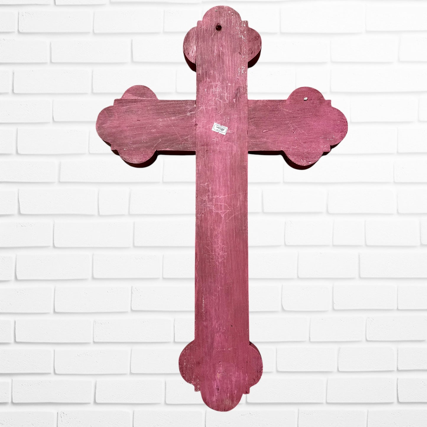 Decorative Milagros wood cross with many charms “miracles” on a white brick wall background Back