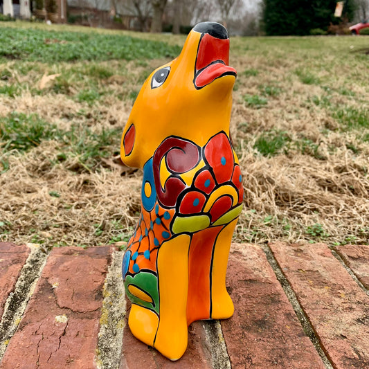 Colorful ceramic coyote figurine on a brick surface with grass in the background