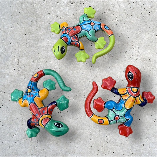 Three colorful talavera ceramic lizards on a textured gray surface