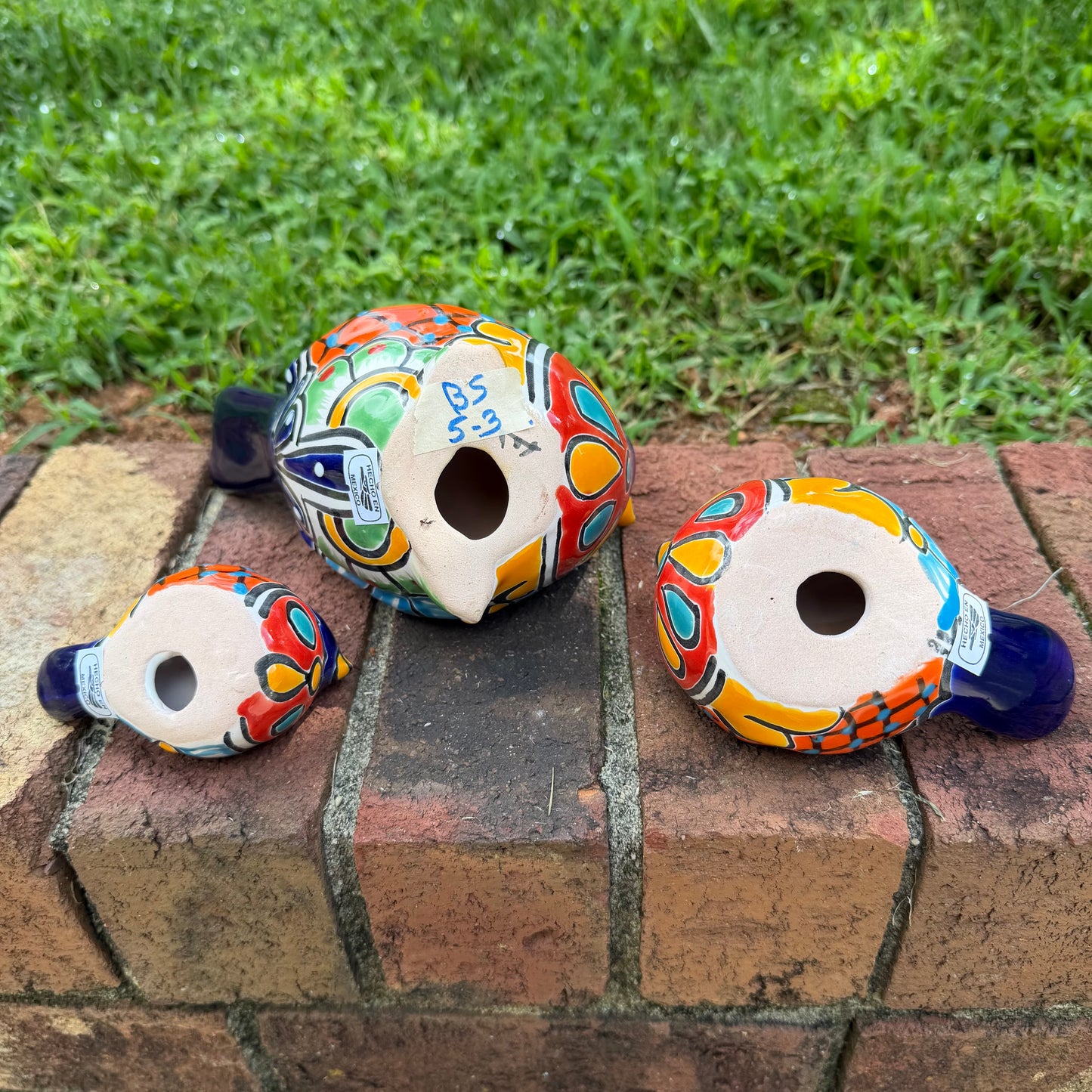 Three hand-painted ceramic bird figurines in different sizes, decorated with a vibrant Mexican Talavera style pattern of blue, red, yellow, and white, bottom view of birds.