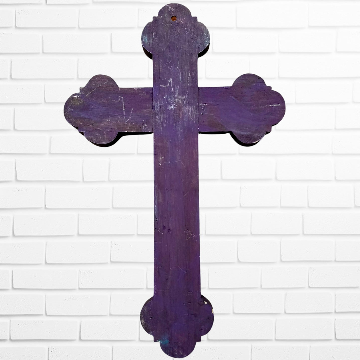 Decorative Milagros wood cross with many charms “miracles” on a white brick wall background Back