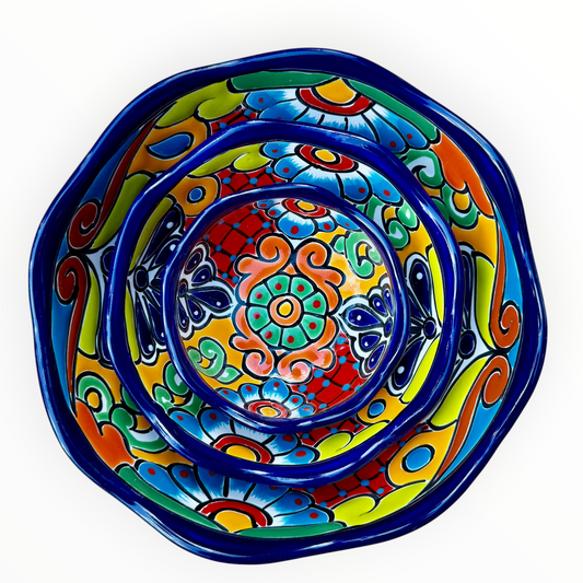 A set of three nested Talavera ceramic bowls with a vibrant hand-painted floral and geometric pattern in multiple colors, featuring a deep blue rim, shown on a plain white background.