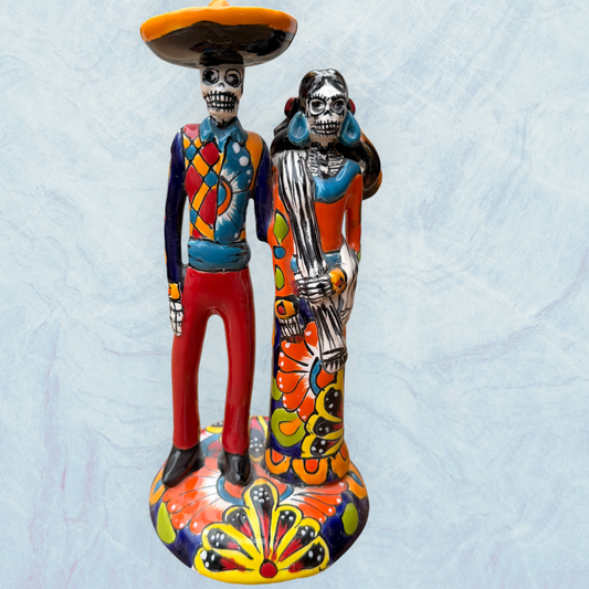 A colorful talavera Skelton cowboy couple standing on a base. He is wearing a big cowboy hat and she has her hair in braids.