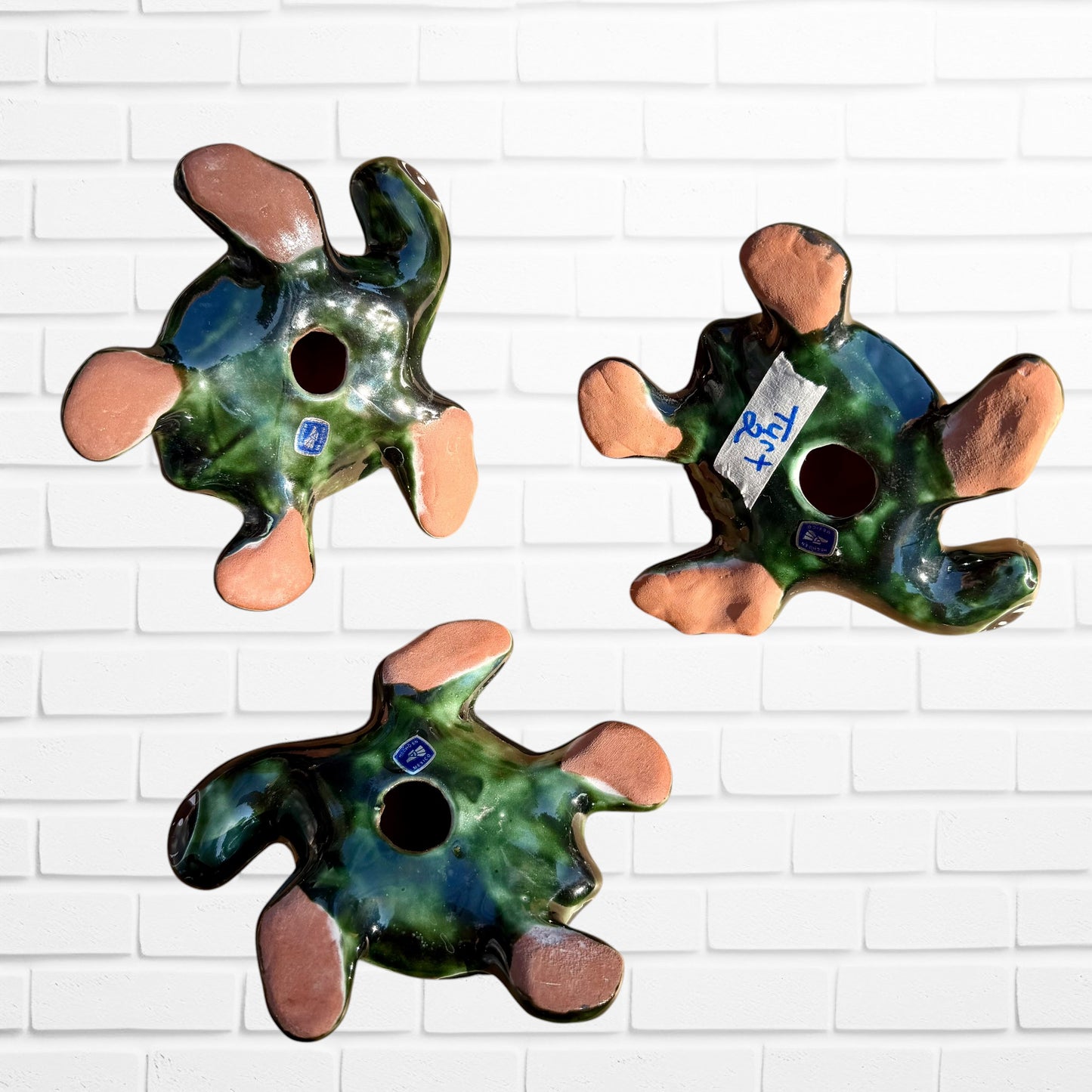Three colorful hand-painted talavera ceramic sea turtles with floral patterns on their shells, displayed against a white brick wall background, back view.