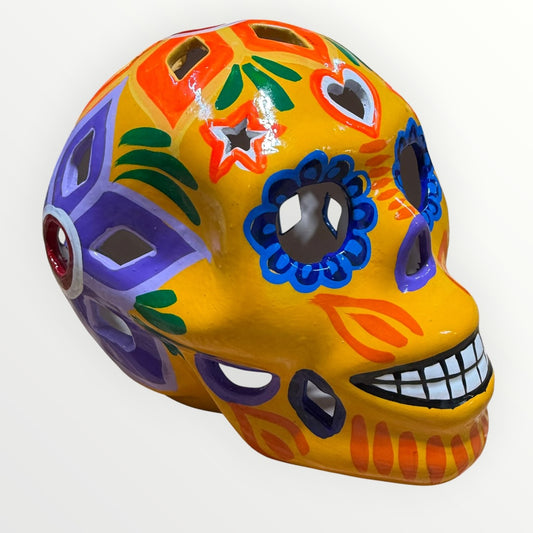 A hand-painted ceramic sugar skull in vibrant yellow, decorated with colorful floral and geometric patterns in blue, purple, green, orange, and red, set against a plain white background.