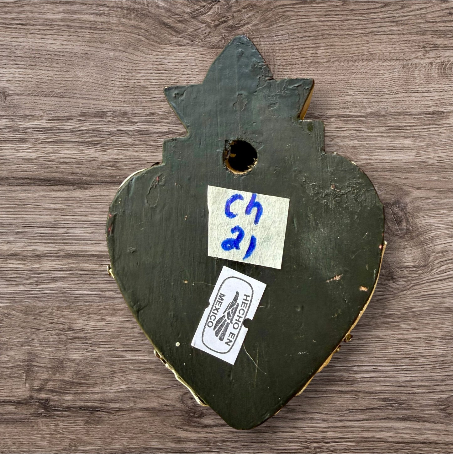 A Mexican Milagros heart in black with a gold flaming top, covered in silver charms, back of heart view.