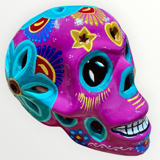 A hand-painted ceramic sugar skull in vibrant purple, turquoise blue, and yellow, decorated with floral and geometric patterns on a plain white background.