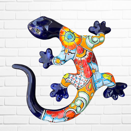 A colorful Talavera ceramic wall sculpture of a salamander, featuring a glossy finish and intricate hand-painted patterns in blue, orange, red, yellow, and white, mounted against a white brick wall, front body view.