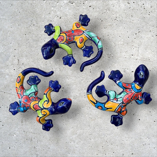 Three colorful talavera ceramic lizards on a textured gray surface