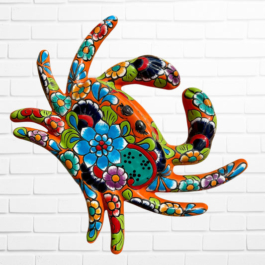 A colorful multicolor hand-painted wall art sculpture of a crab, decorated with vibrant floral patterns, shown against a white brick wall background.