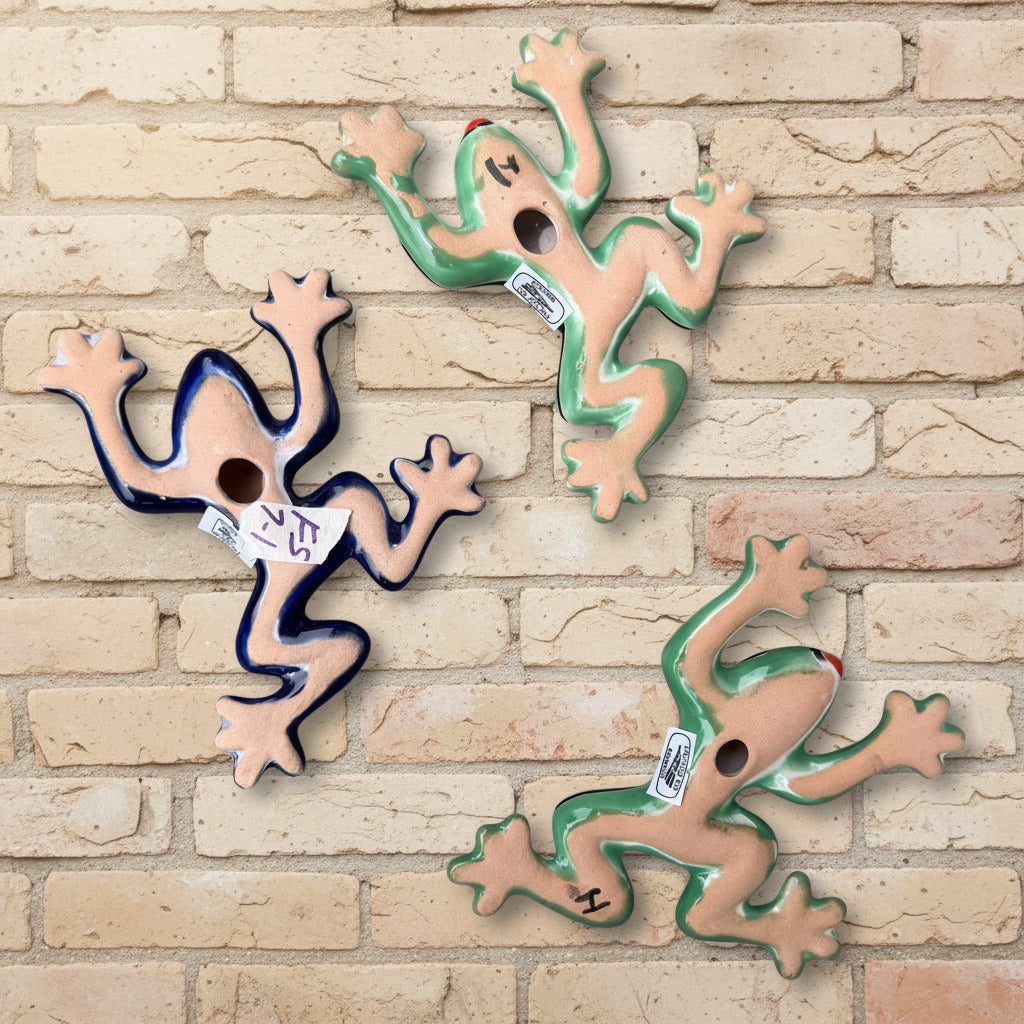 Three colorful ceramic wall-mounted frog sculptures in a vibrant multicolor design, displayed against a white brick wall background back view showing hanging hole.