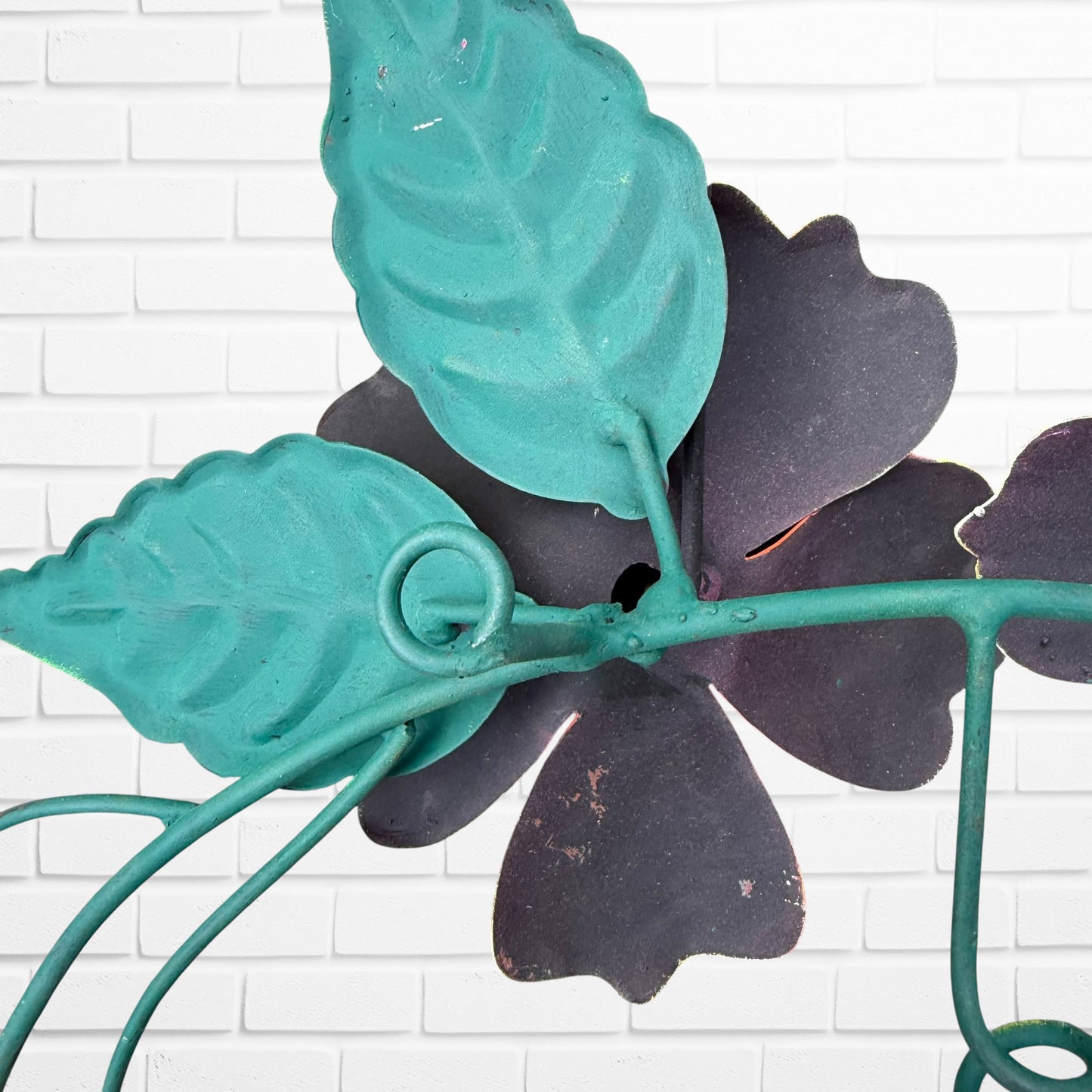 Decorative wall art with three orange flowers and hummingbird on a white brick wall background close up of hanging hook.
