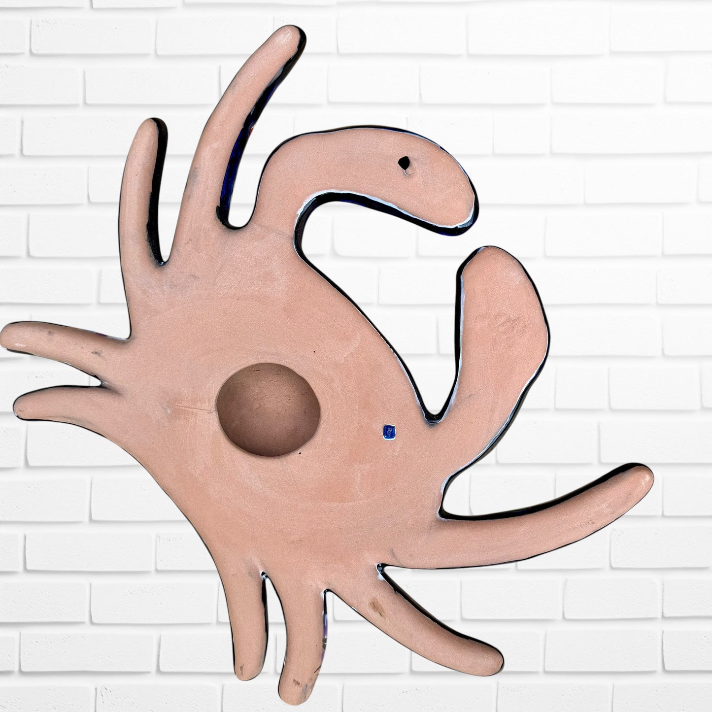 A colorful talavera crab wall art sculpture decorated with vibrant floral patterns, shown against a white brick wall background, back view of Crab.