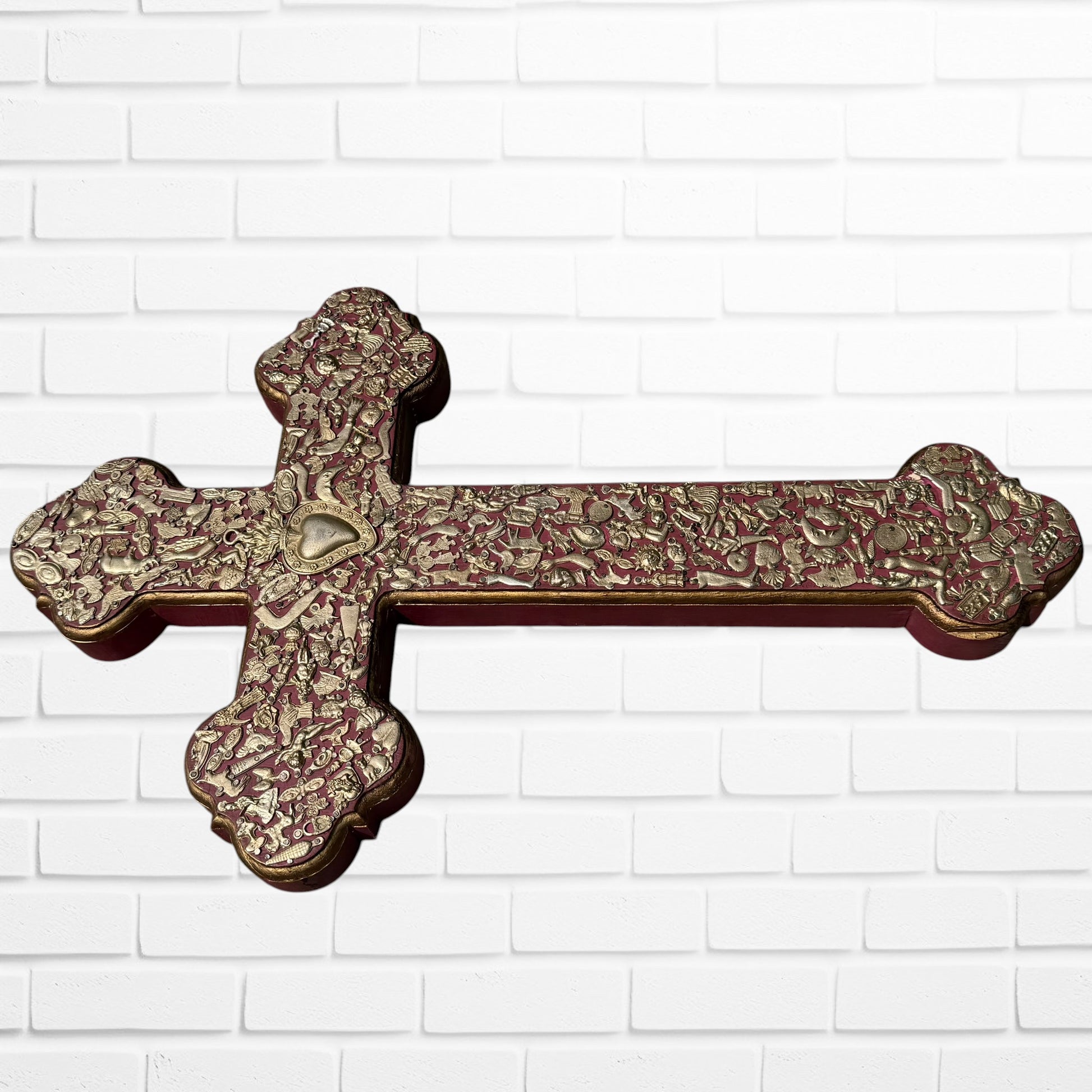 Decorative Milagros wood cross with many charms “miracles” on a white brick wall background Left side