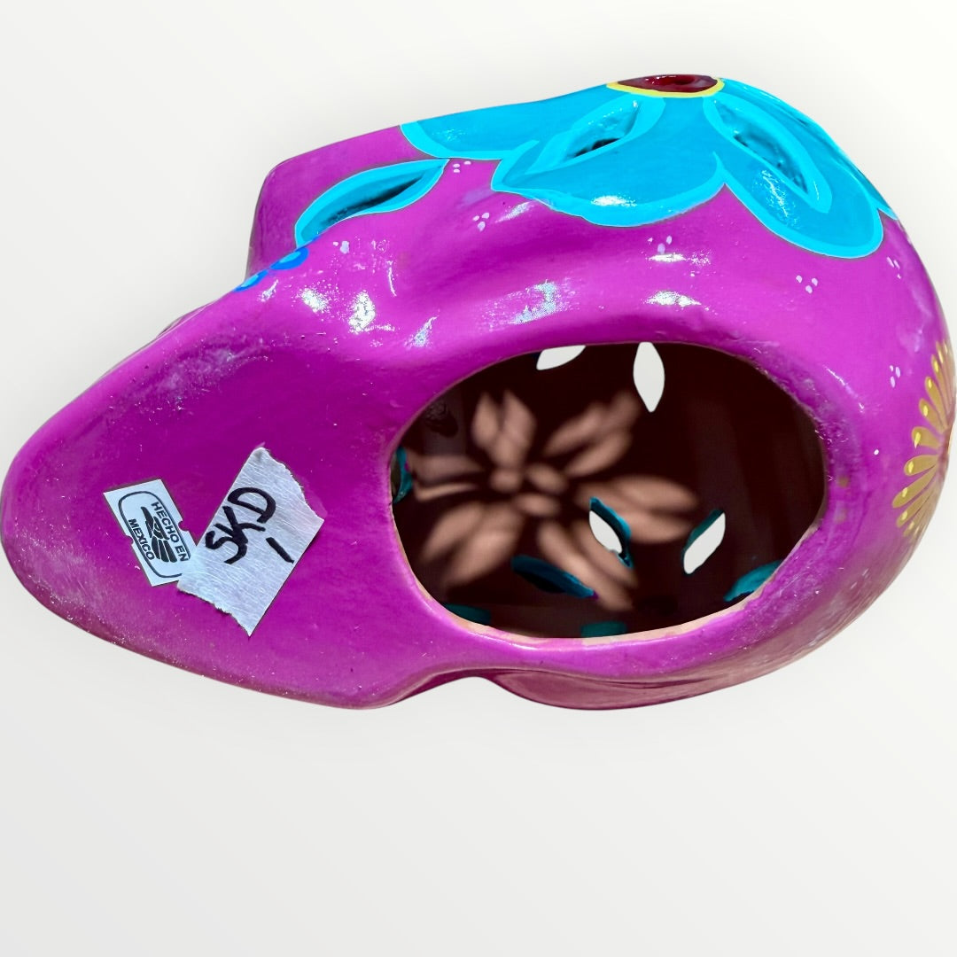 A hand-painted ceramic sugar skull in vibrant purple, turquoise blue, and yellow, decorated with floral and geometric patterns on a plain white background bottom view.