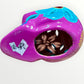 A hand-painted ceramic sugar skull in vibrant purple, turquoise blue, and yellow, decorated with floral and geometric patterns on a plain white background bottom view.