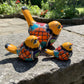 Three hand-painted ceramic bird figurines in yellow, decorated with intricate blue, black, red, green, and orange floral patterns, arranged on a rustic wooden surface left side view