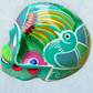 A decorative skull sculpture with intricate colorful sugar skull style patterns painted on a teal colored base, set against a light blue textured background, right side view.
