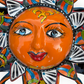 A colorful hand-painted Talavera ceramic sun wall decor piece with a smiling face, orange center, planets, and multicolored rays on a plain white background face close up.