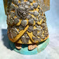 Milagros wooden guardian angel figurine wearing a yellow robe with gold and silver metallic details, standing on a light blue textured background, Close up of the gown, bottom and bare feet.