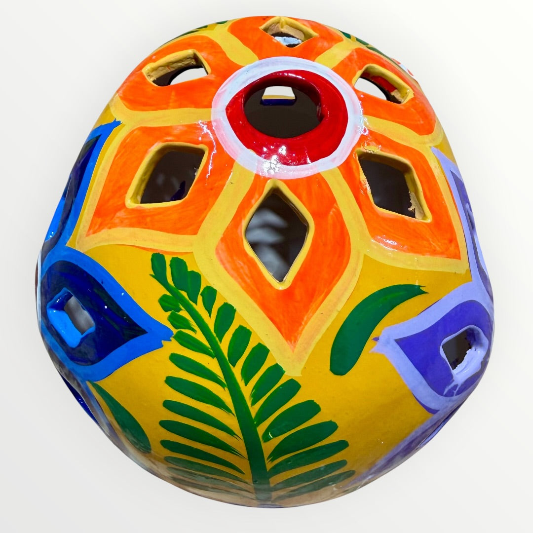 A hand-painted ceramic sugar skull in vibrant yellow, decorated with colorful floral and geometric patterns in blue, purple, green, orange, and red, set against a plain white background top cut outs.