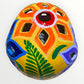 A hand-painted ceramic sugar skull in vibrant yellow, decorated with colorful floral and geometric patterns in blue, purple, green, orange, and red, set against a plain white background top cut outs.