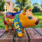A colorful hand-painted yellow Talavera pig figurine standing on a brick surface with a blurred outdoor garden background.