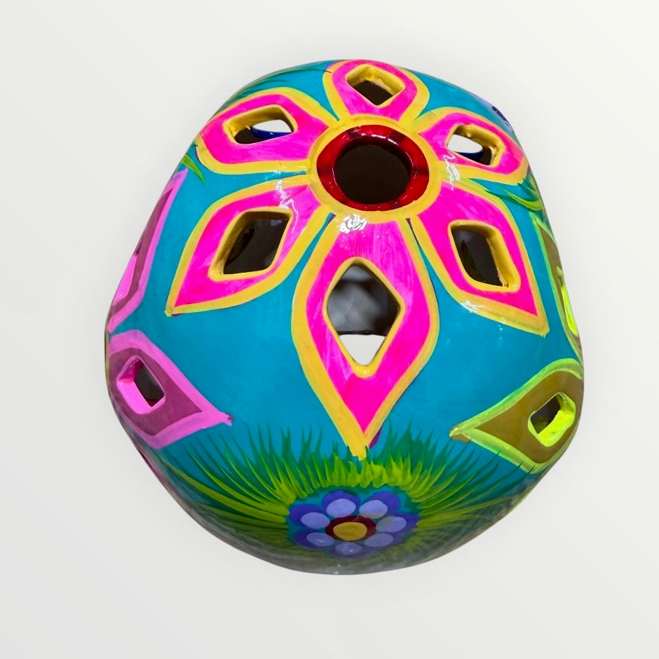 A decorative sugar skull painted in bright turquoise blue with colorful floral and geometric patterns in pink, yellow, green, purple, and white, shown against a plain light background top cut outs