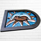 Decorative wall art of a sun and moon face with a metal frame on a white brick wall. Designed by artist Andres Martin right side view