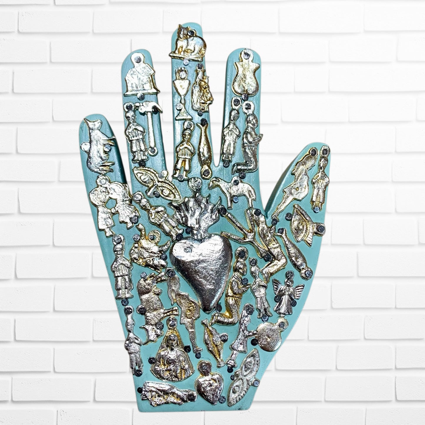 Decorative wall art in the shape of a hand with various small figurines and a heart on a white brick background light blue two