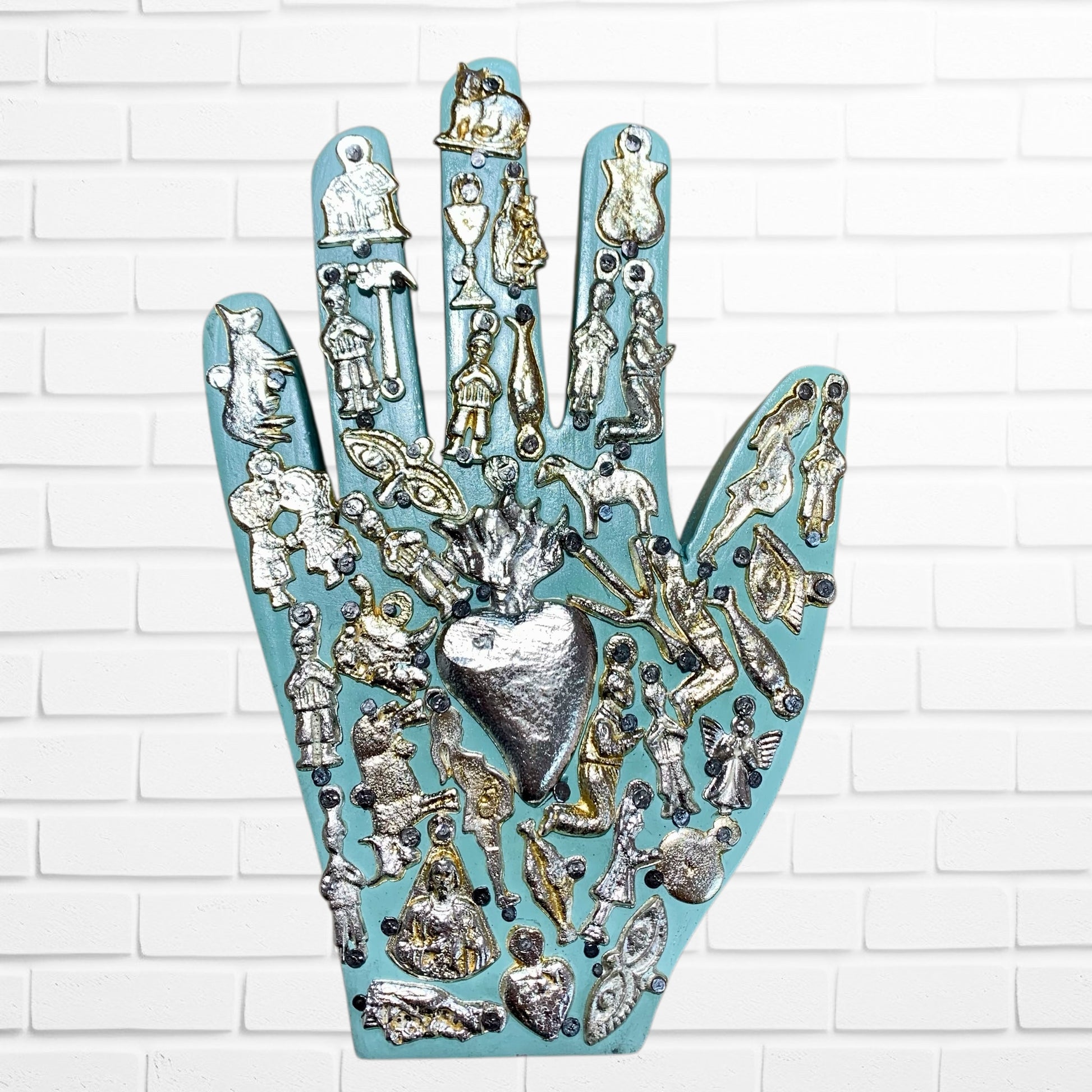 Decorative wall art in the shape of a hand with various small figurines and a heart on a white brick background light blue two