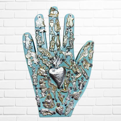 Decorative wall art in the shape of a hand with various small figurines and a heart on a white brick background light blue two
