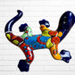 A colorful, glossy lizard wall sculpture with 
a vibrant mosaic pattern of blue, orange, yellow, green, red, and black, mounted on a white brick wall back view.