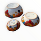 A set of nested, round Talavera ceramic bowls decorated with a vibrant, hand-painted Mexican Talavera style pattern featuring blue, yellow, orange, red, and green designs on a white background, bottom side view.