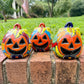 Three hand-painted Talavera ceramic jack-o'-lantern pumpkins with orange faces and yellow, blue, and red green designs, sitting on a brick path in a grassy backyard.
