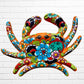 A colorful multicolor hand-painted wall art sculpture of a crab, decorated with vibrant floral patterns, shown against a white brick wall background, top shell.