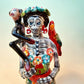 A Talavera Day of the Dead (Día de los Muertos) Frida figurine  with a monkey on her shoulder and a red parrot on her other shoulder, set against a light blue gradient background. Close up of Frida’s face.