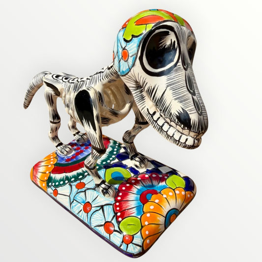 A talavera catrina dog skeleton figurine with colorful hand-painted floral and geometric patterns, standing on a matching decorated base against a plain white background.
