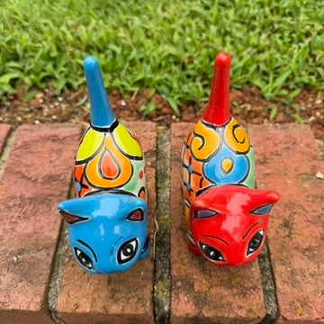 Two hand-painted Mexican-style ceramic cat figurines, one blue and one red, decorated with colorful geometric patterns, standing on a brick surface outdoors top view
