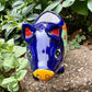 Colorful Talavera ceramic pig planter on a stone surface with green plants in the background Face view