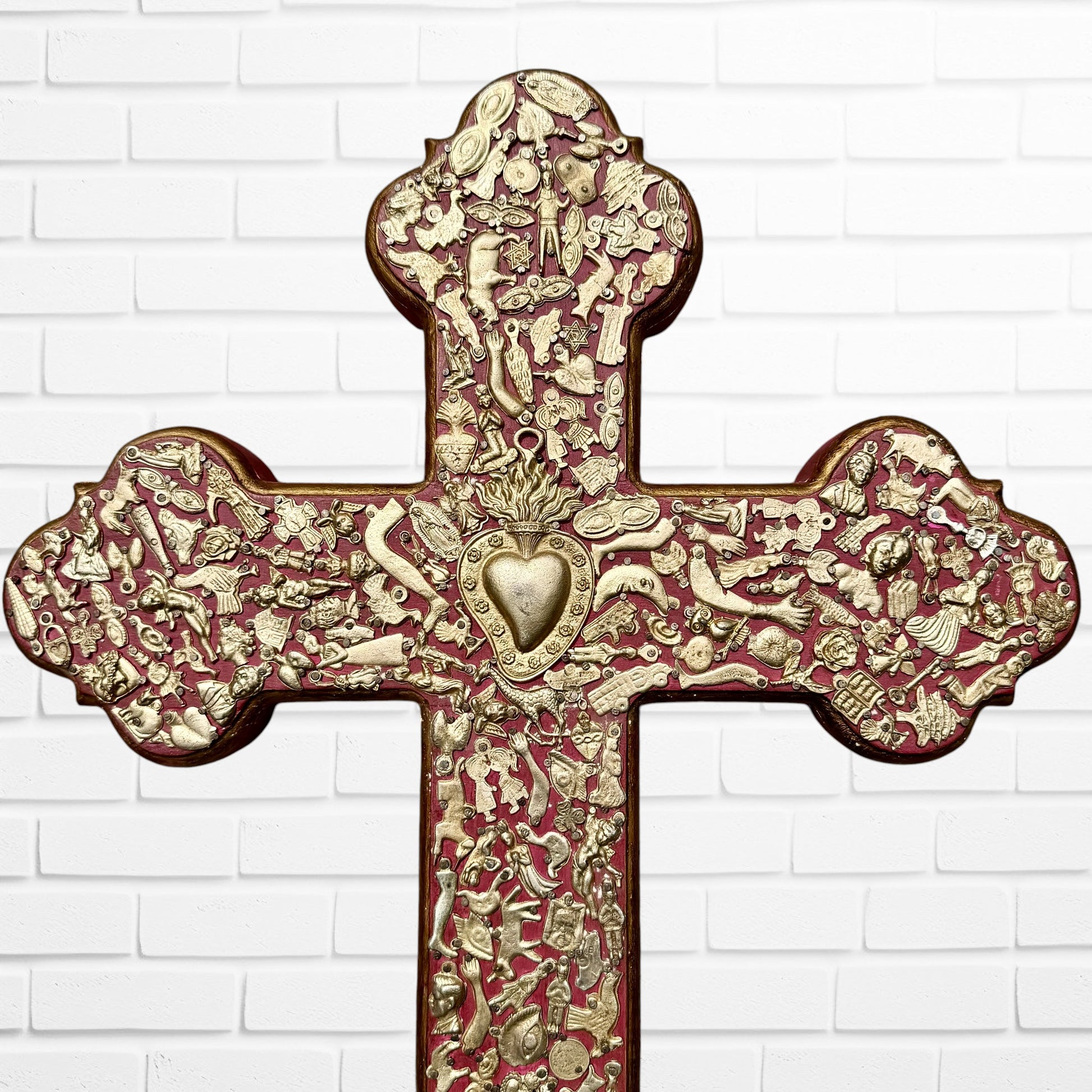 Decorative Milagros wood cross with many charms “miracles” on a white brick wall background Top half