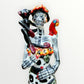 A Day of the Dead Catrina of a Frida skeleton doll holding a black cat, with a red parrot on her shoulder and colorful flowers around the top of her dress.