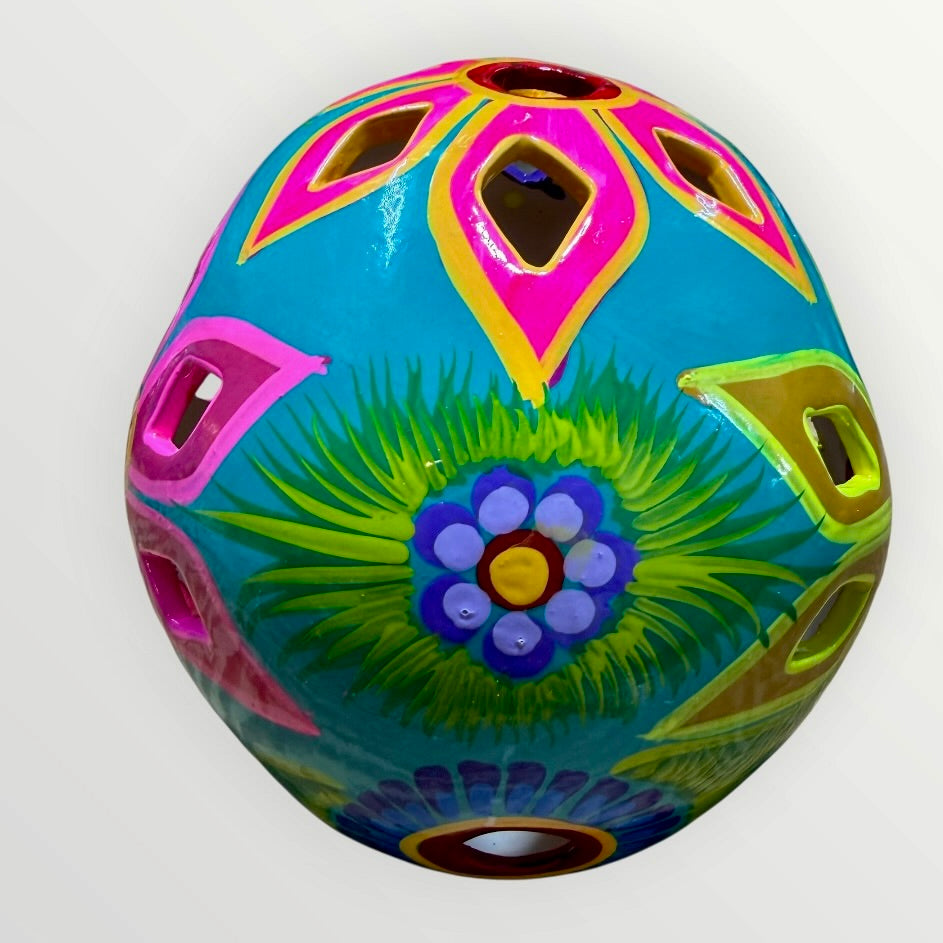 A decorative sugar skull painted in bright turquoise blue with colorful floral and geometric patterns in pink, yellow, green, purple, and white, shown against a plain light background back view