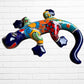 A colorful ceramic wall sculpture of a stylized lizard, decorated with vibrant hand-painted patterns in blue, orange, green, yellow, and red, mounted on a white brick wall front view