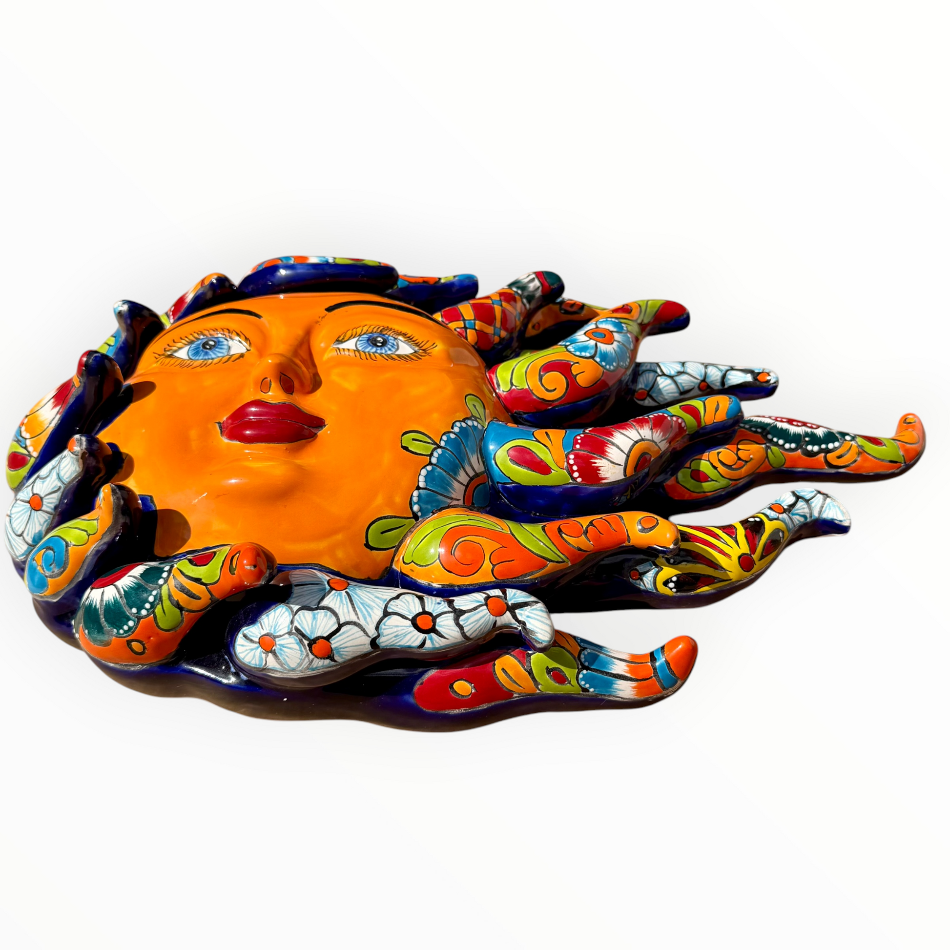 A colorful hand-painted Talavera ceramic sun wall sculpture with big wavy rays on a plain white background, view from the bottom.