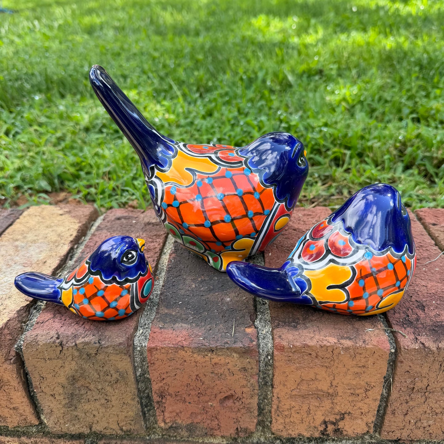 Three hand-painted ceramic bird figurines in different sizes, decorated with a vibrant Mexican Talavera style pattern of blue, red, yellow, and white, showing left side view

