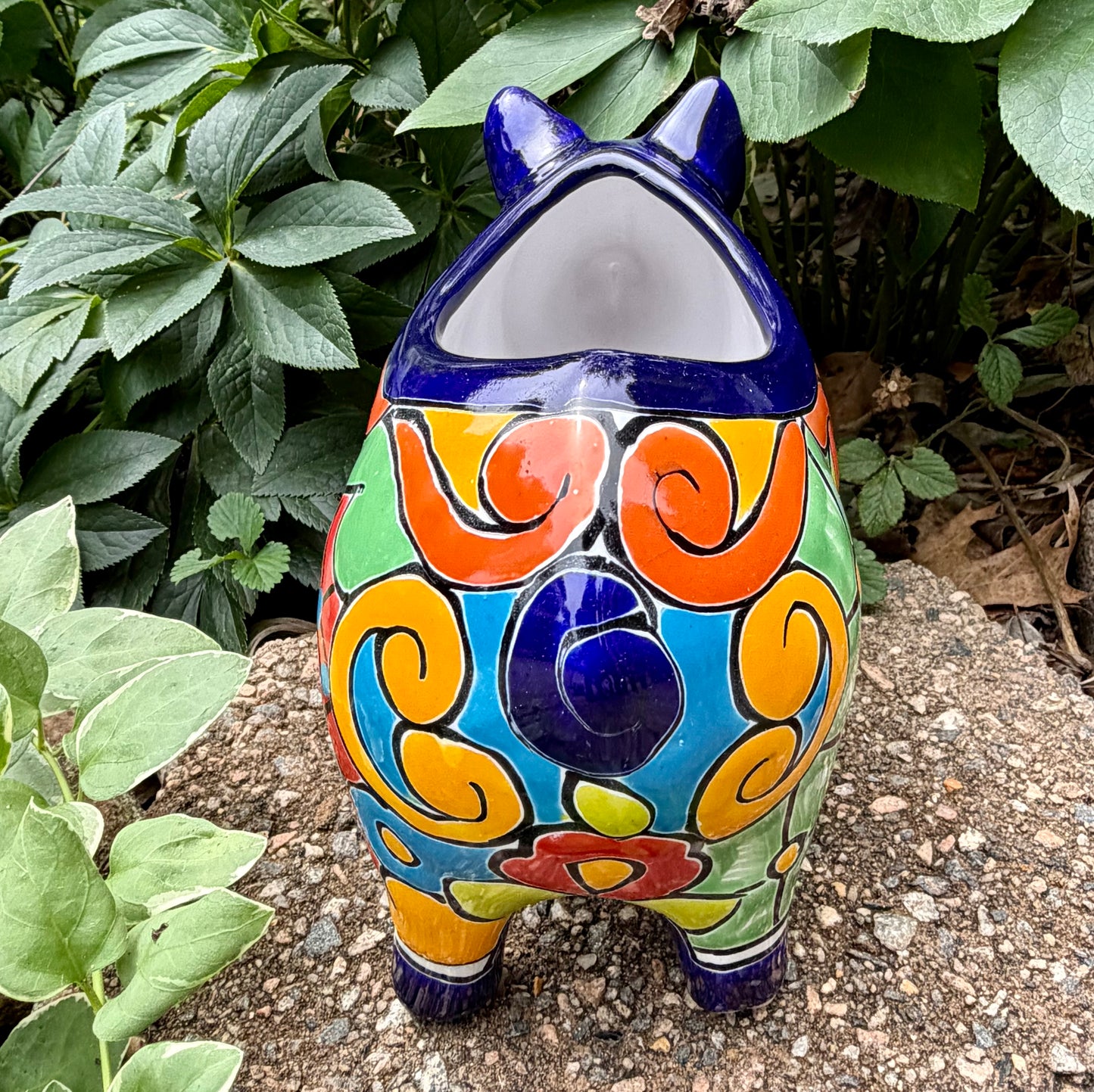 Colorful Talavera ceramic pig planter on a stone surface with green plants in the background Back