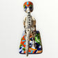 A ceramic Mexican-style skeleton dog figurine standing on a colorful floral base against a plain white background. Back view of dog showing backbone.
