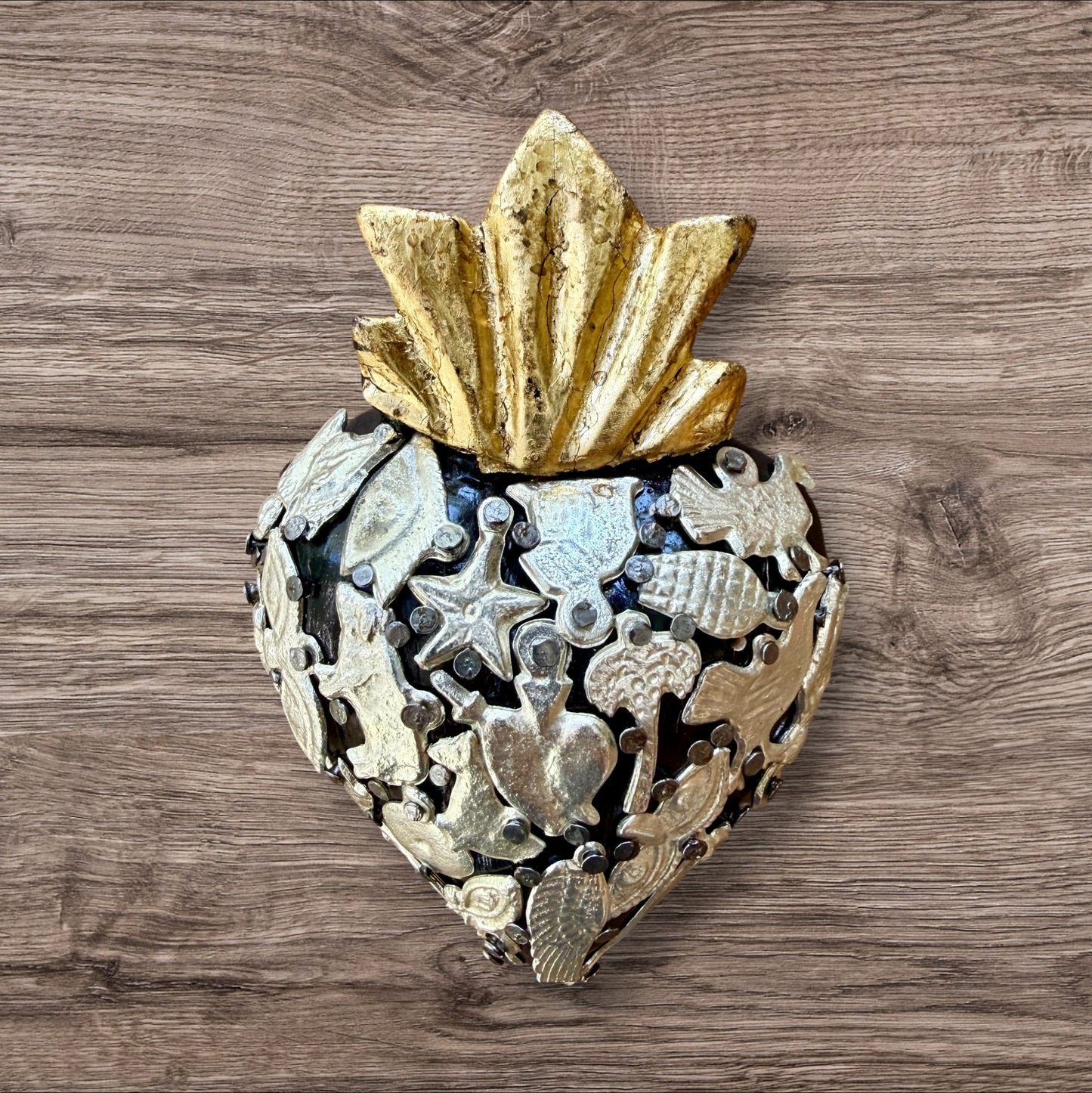 A Mexican Milagros heart in black with a gold flaming top, covered in antiqued charms. 
